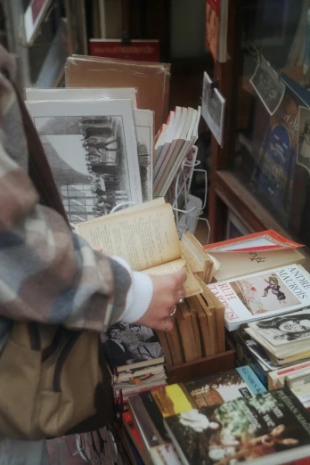 a person standing in front of a table full of books, old shops, zoomed in, looking down, vendors