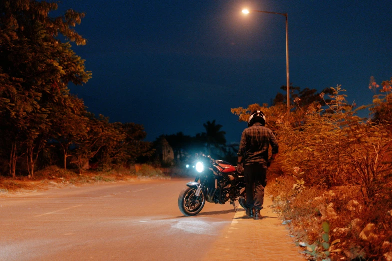 a man standing next to a motorcycle on a dirt road, during night, profile image, technical, on an indian street