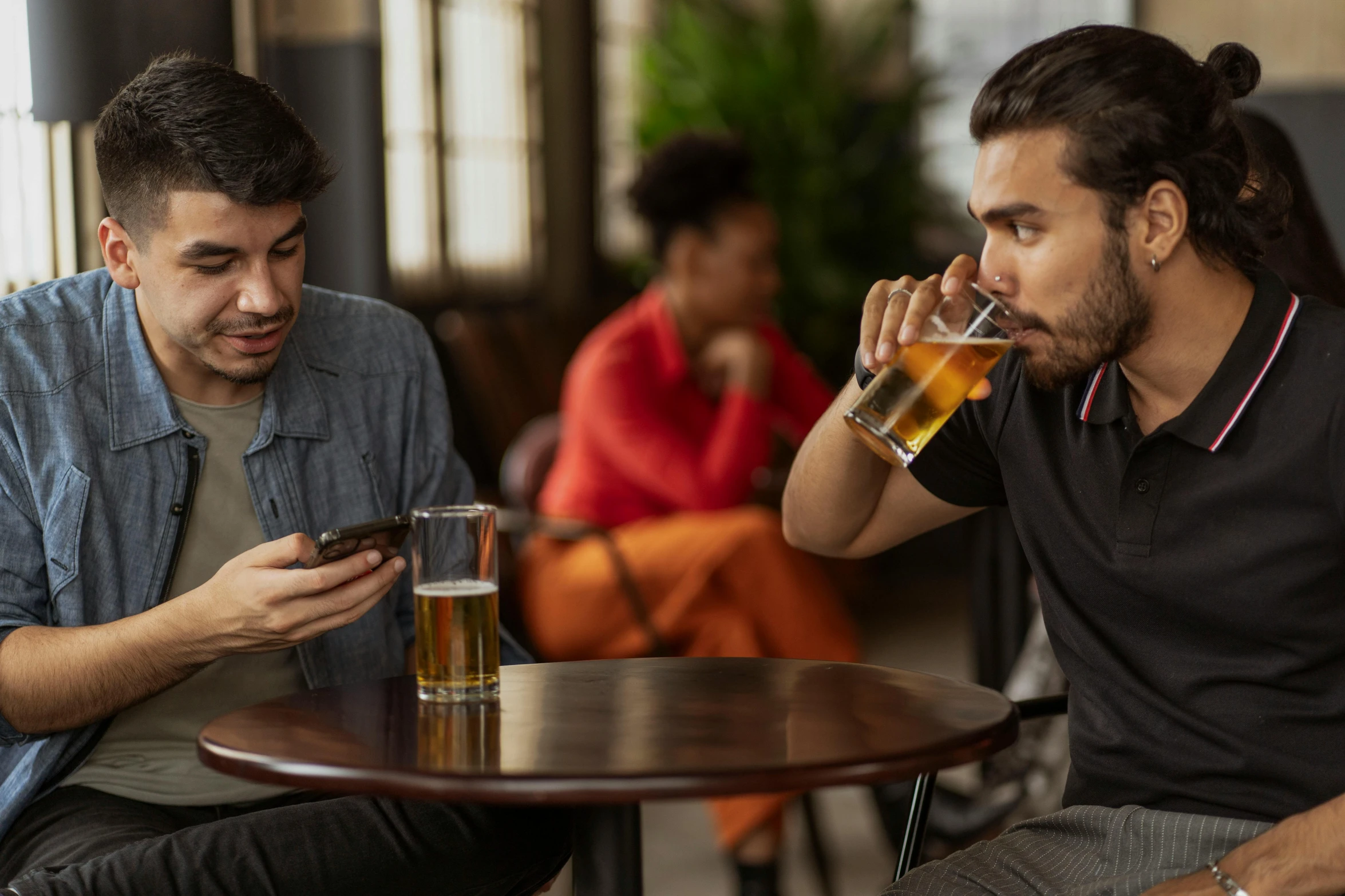 two men sitting at a table drinking beer and looking at their cell phones, a photo, shutterstock, 😭🤮 💔, flirting, sitting in a lounge, holding the pint of ale