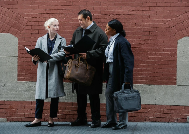 a group of people standing in front of a brick wall, lawyer, portfolio, raising between the buildings, collaboration