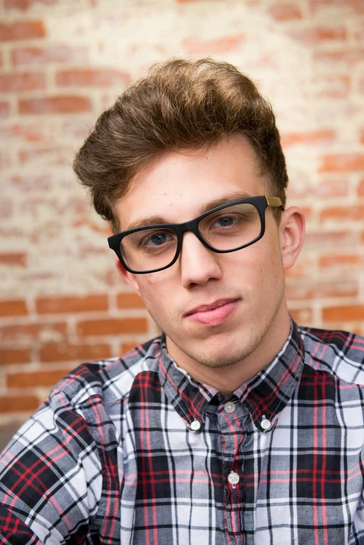 a young man wearing glasses sitting in front of a brick wall, inspired by Ryan Pancoast, shutterstock, photorealism, square glasses, clean shaven wide face, rhett and link, 15081959 21121991 01012000 4k