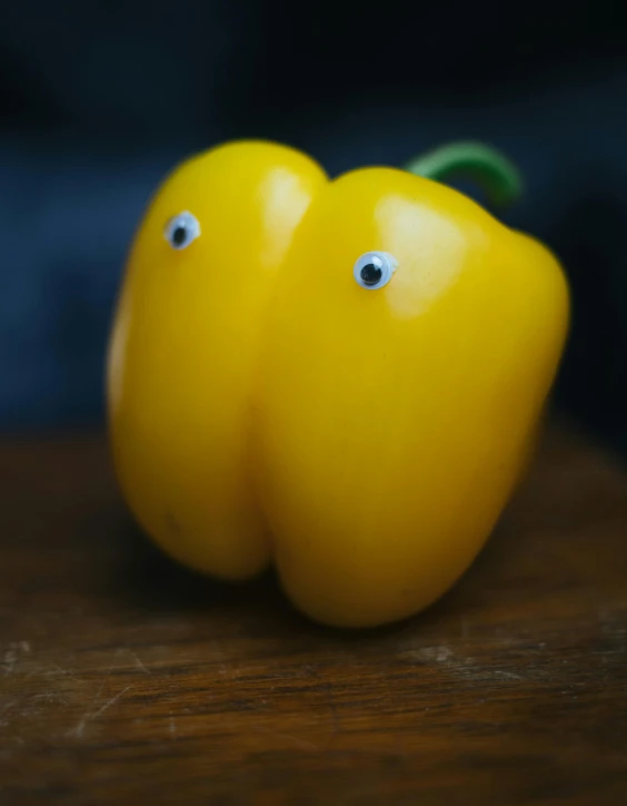 a couple of yellow peppers sitting on top of a wooden table, inspired by Tomi Ungerer, unsplash, happening, eyes in the style of nendoroid, close up front view, multicoloured, dan munford