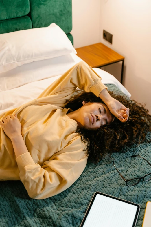 a woman laying on top of a bed next to a laptop, inspired by Elsa Bleda, trending on pexels, renaissance, concerned, brown curly hair, wearing nanotech honeycomb robe, walking down