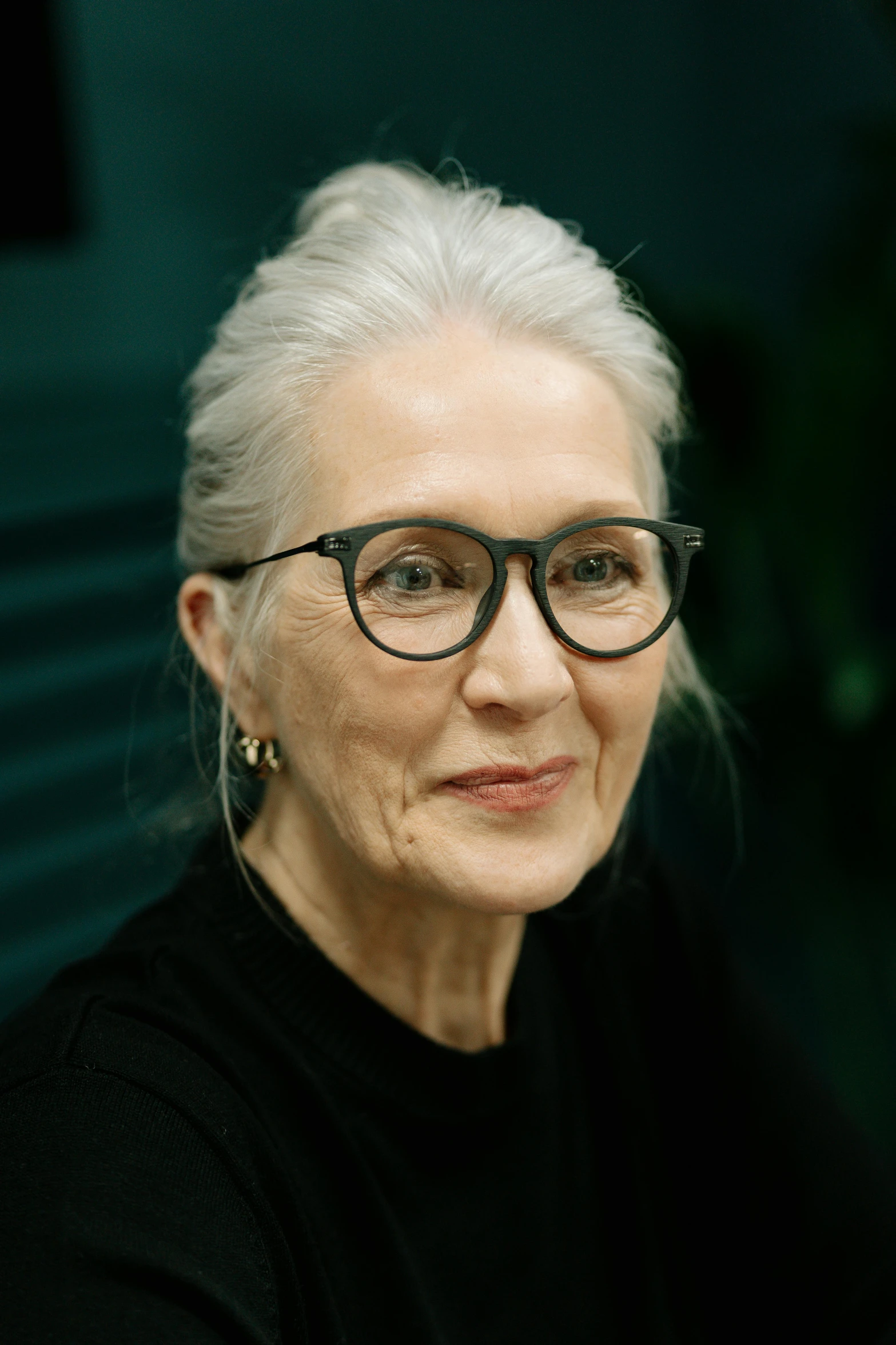 a woman with glasses sitting at a table, straight grey hair, marie - gabrielle capet style, lovingly looking at camera, profile image