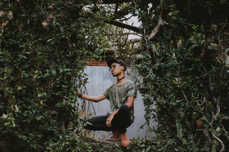 a man standing in the middle of a lush green forest, an album cover, by Emma Andijewska, pexels contest winner, visual art, sitting in the garden, ashteroth, non binary model, branches and ivy