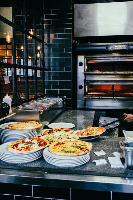 a man that is standing in front of some pizzas, a photo, by Julia Pishtar, trending on unsplash, charcoal and silver color scheme, at the counter, chef table, “ iron bark