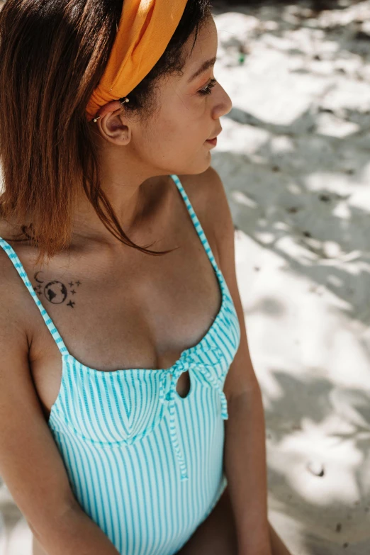 a woman sitting on top of a sandy beach, a tattoo, trending on pexels, striped orange and teal, close up bust shot, one piece style, seafoam green