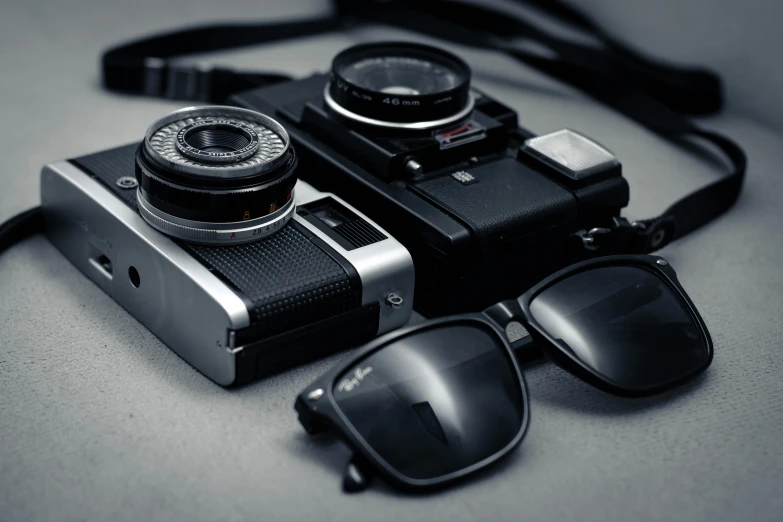 a pair of sunglasses and a camera on a table, a black and white photo, rolleiflex tlr, glasses, lenses