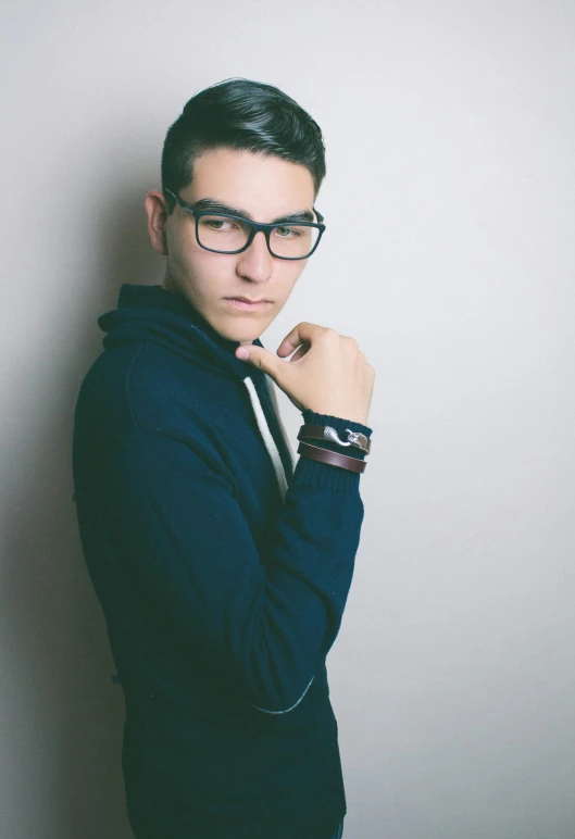 a man wearing glasses leaning against a wall, inspired by Josh Bayer, hasan piker, profile image, non binary model, crossed arms