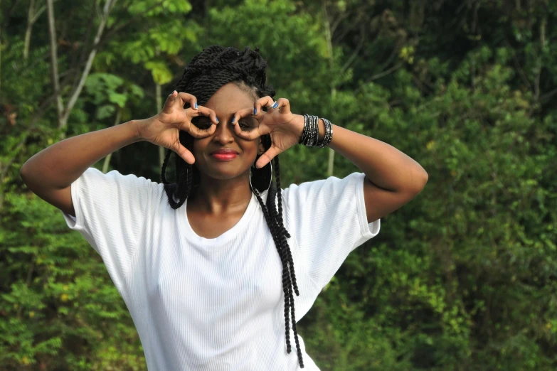 a woman making a heart with her hands, inspired by Chinwe Chukwuogo-Roy, pexels contest winner, afrofuturism, eyes in the trees, dressed in a white t shirt, doing a sassy pose, adinkra symbols