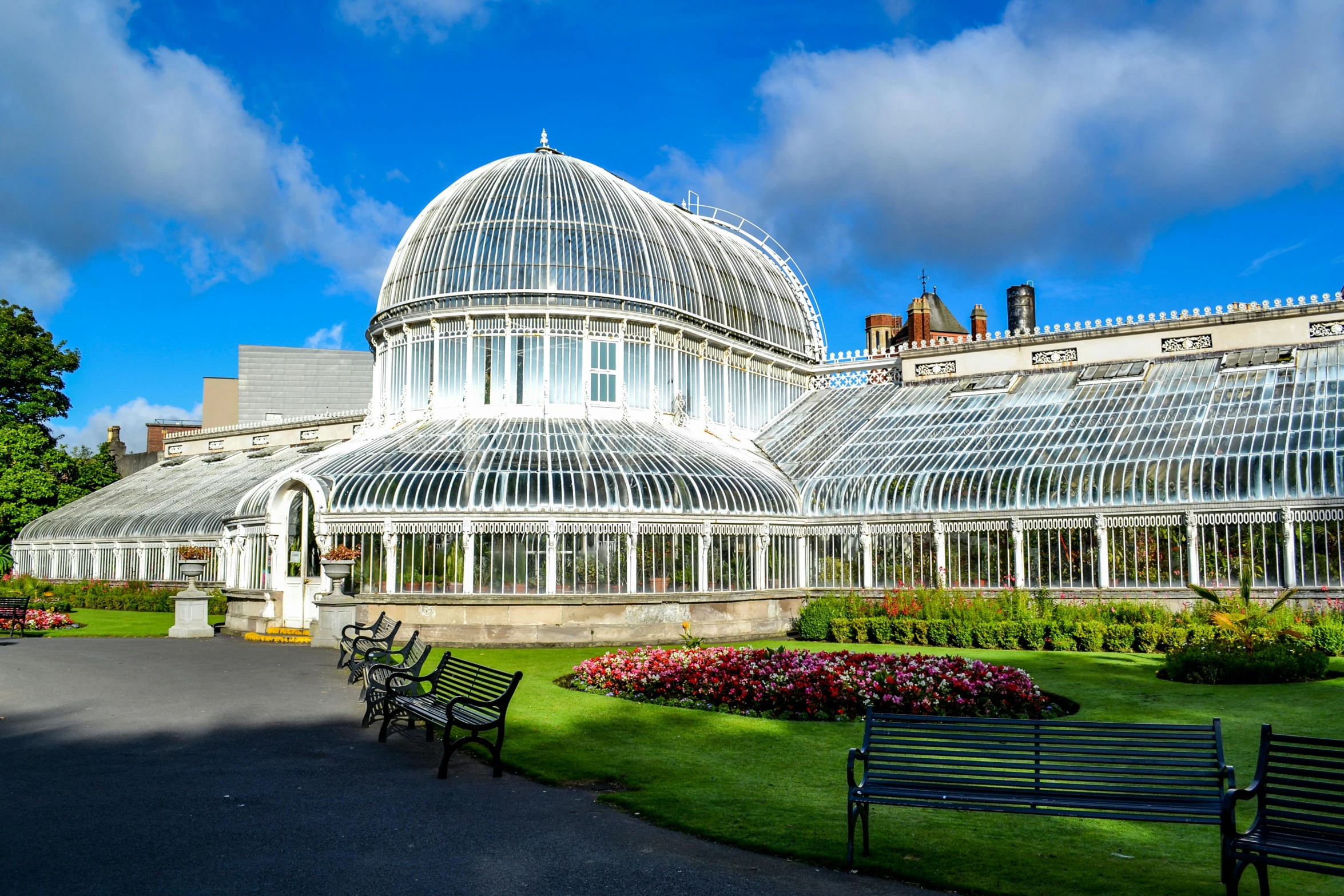 a large glass greenhouse sitting on top of a lush green field, inspired by Edwin Deakin, art nouveau, with palm trees and columns, glasgow, white stone arches, neon city domes