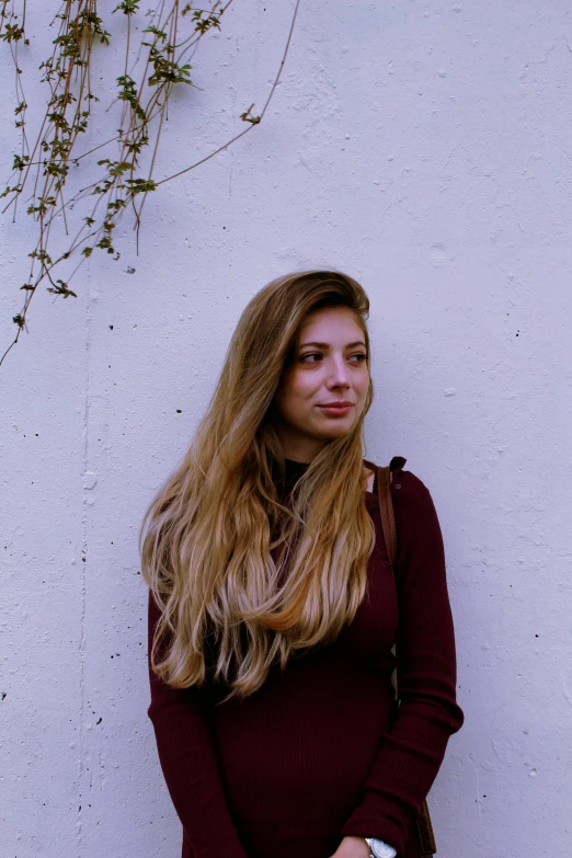 a woman standing in front of a white wall, inspired by Elsa Bleda, renaissance, dark blond long hair, around 1 9 years old, purple hue, slightly smiling