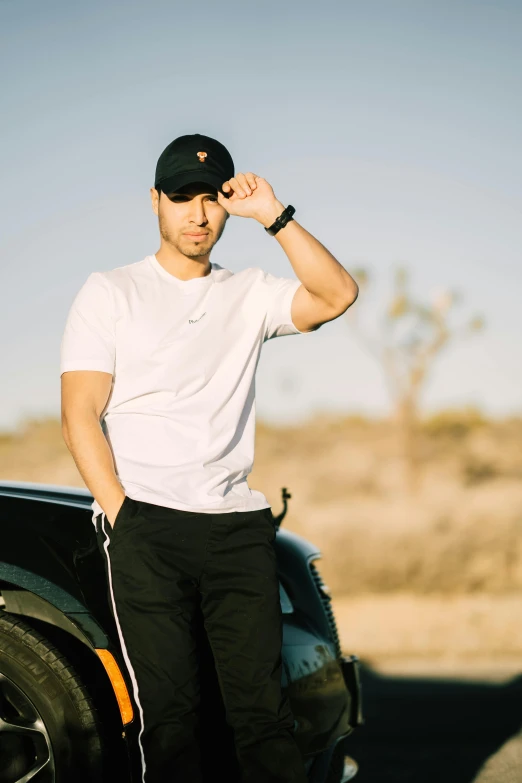 a man standing next to a car in the desert, by Robbie Trevino, wearing a black t-shirt, daniel ricciardo, profile image, black hat