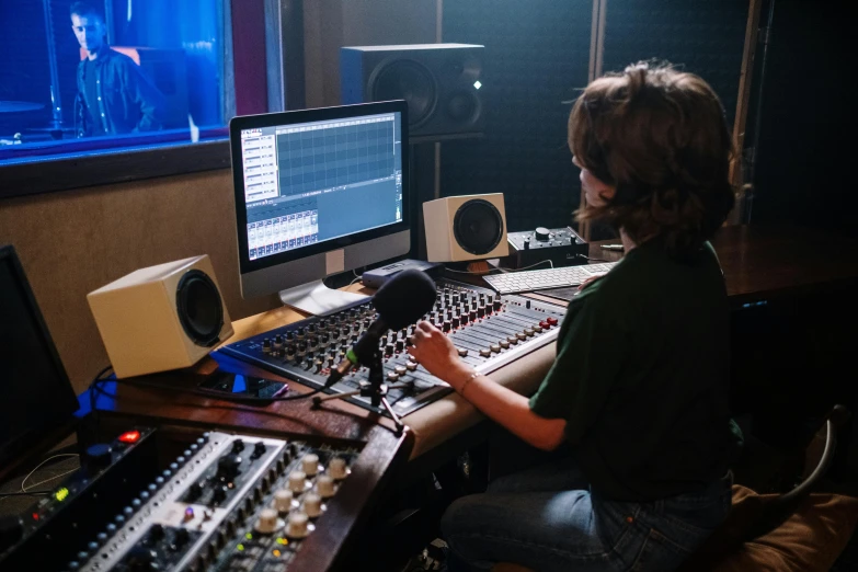 a person sitting at a desk in front of a computer, an album cover, by Dan Content, shutterstock, standing microphones, studio room, theatre equipment, sitting at a control center