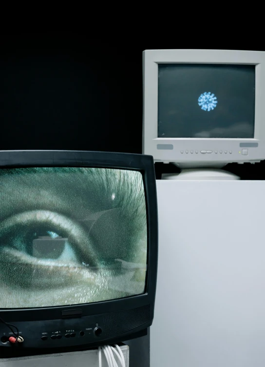 a television sitting on top of a desk next to a monitor, inspired by David Wojnarowicz, video art, close - up shot of eyes, electron microscope view, 1 9 8 0 s computers, trapped egos in physical reality