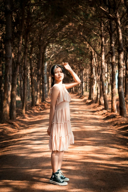 a woman standing in the middle of a forest, inspired by Jung Park, pexels contest winner, renaissance, korean women's fashion model, ((((dirt brick road)))), light dress, in shades of peach