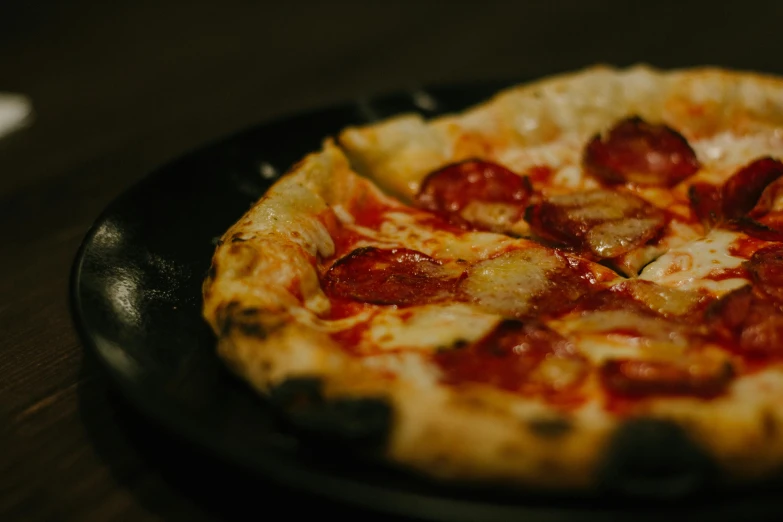 a pepperoni pizza sitting on top of a black plate, by Tom Bonson, unsplash, woodfired, aged 2 5, vanilla, battered