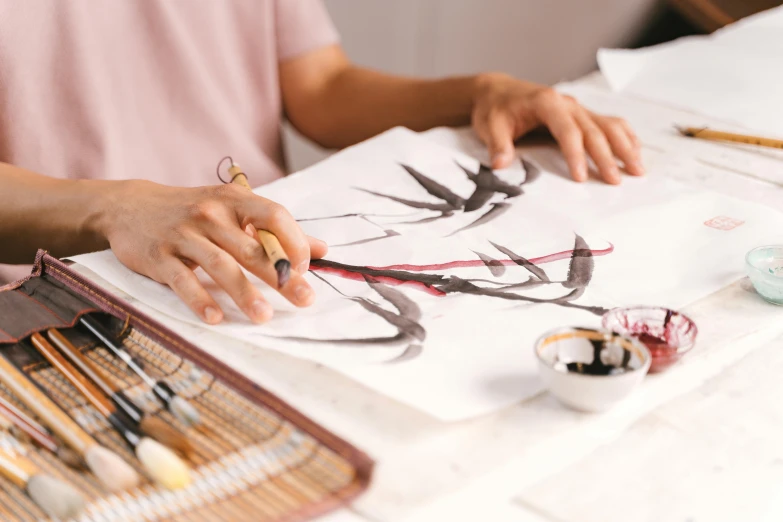 a woman sitting at a table painting on a piece of paper, inspired by Qi Baishi, trending on pexels, origami crane drawings, intricate brush stroke detail, on a white table, on a canva