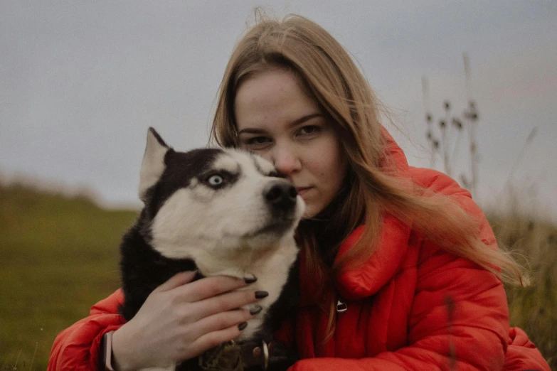 a woman in a red jacket hugging a black and white dog, pexels contest winner, realism, siberian husky, avatar image, handsome girl, model wears a puffer jacket