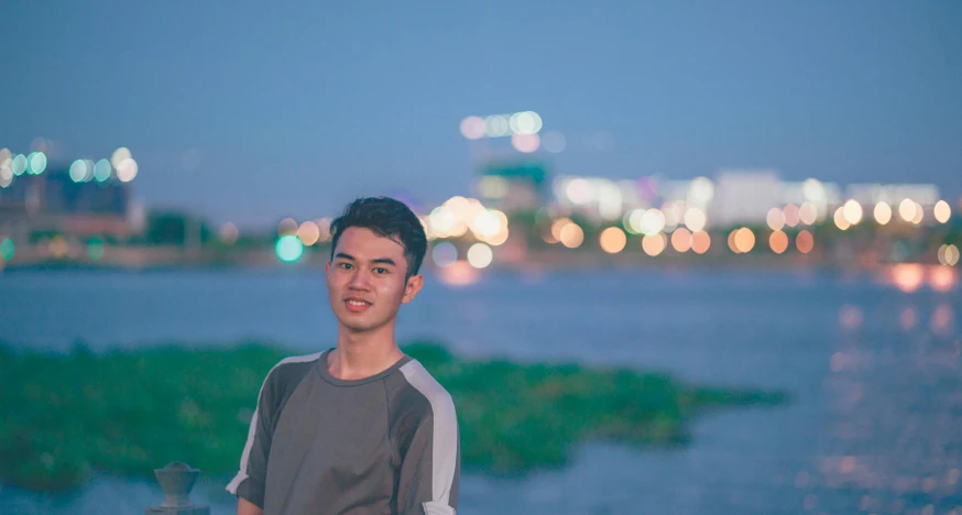 a man standing in front of a body of water, a picture, set on singaporean aesthetic, avatar image, good lighted photo, slight friendly smile