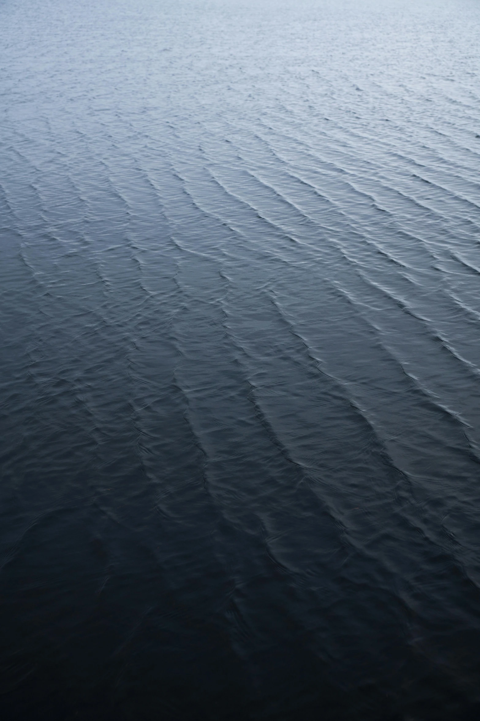 an aerial view of a body of water, ripples, hues of subtle grey, dark ocean, even surface