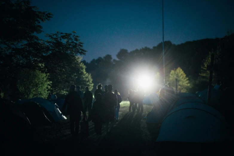 a group of people that are standing in the dark, campsites, floodlight, lights in distance, sun overhead