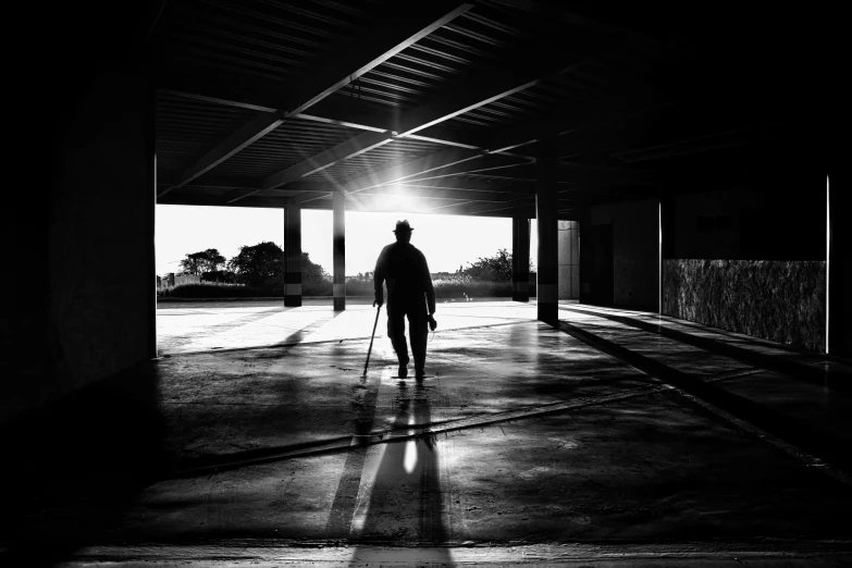 a black and white photo of a person walking in a building, sun behind him, holding walking stick, outside in parking lot, awarded on cgsociety