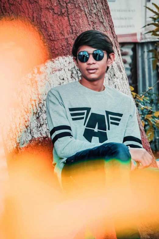 a man sitting next to a tree wearing sunglasses, inspired by Rudy Siswanto, aestheticism, wearing sweatshirt, ansel ], teenage, coloured photo