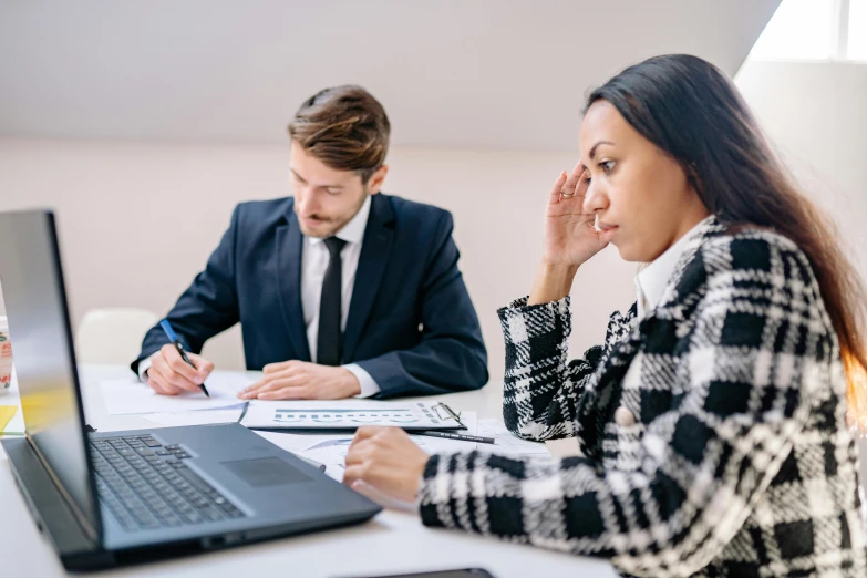 a couple of people sitting at a table with a laptop, sat in an office, downward somber expression, avatar image, professional image