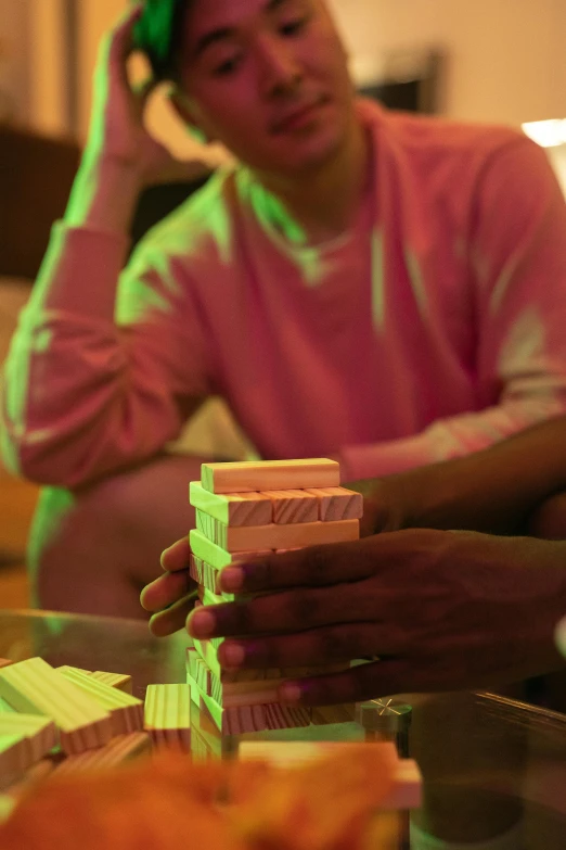a man sitting at a table with food in front of him, pexels contest winner, process art, jenga tower, pastel pink neon, playing cards, cinematic closeup