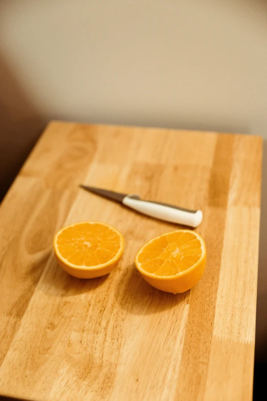 an orange sitting on top of a cutting board next to a knife, sitting on a table, medium angle, bottom angle, on display