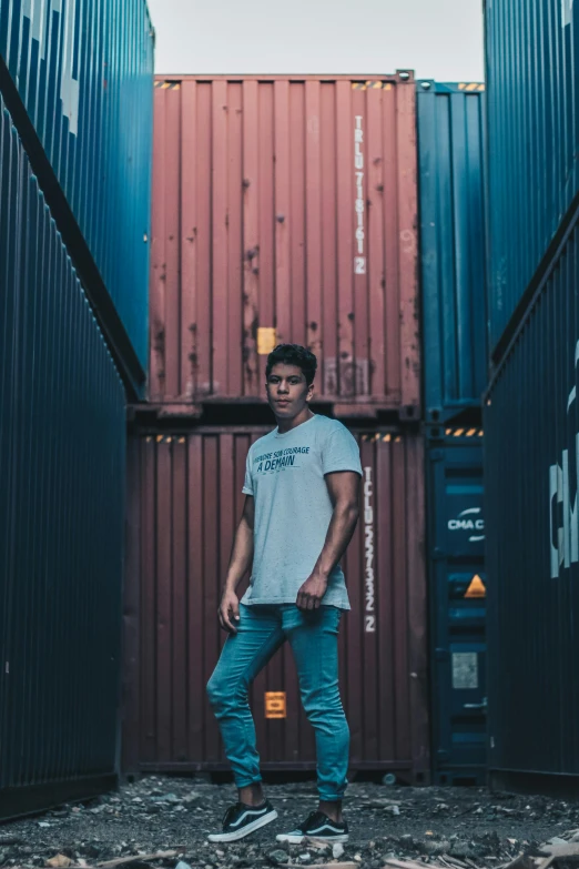 a man standing in front of a stack of shipping containers, an album cover, pexels contest winner, wearing pants and a t-shirt, headshot profile picture, 5 0 0 px models, asher duran