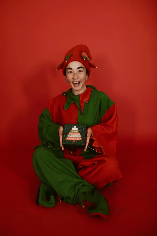 a boy wearing a red and green elf outfit while sitting down