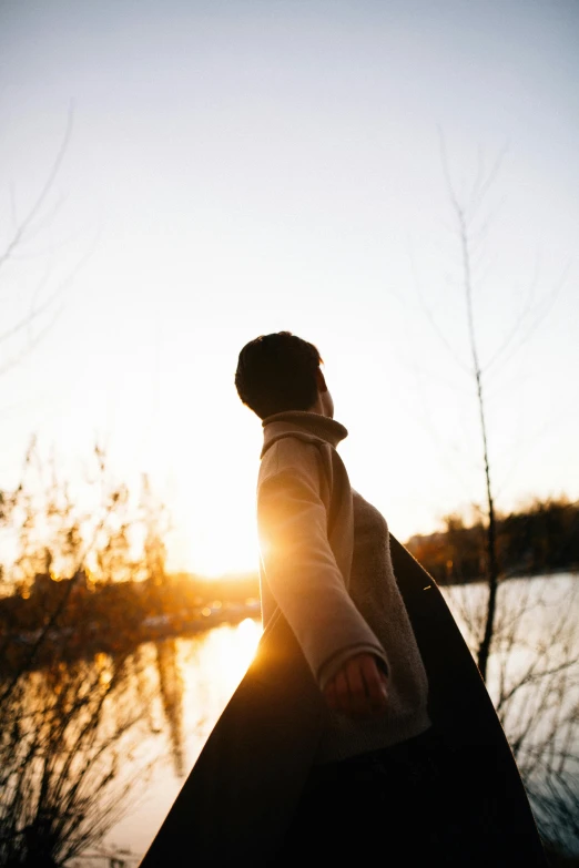 a person standing next to a body of water, trending on pexels, winter sun, embrace the superego, spring evening, low - angle shot
