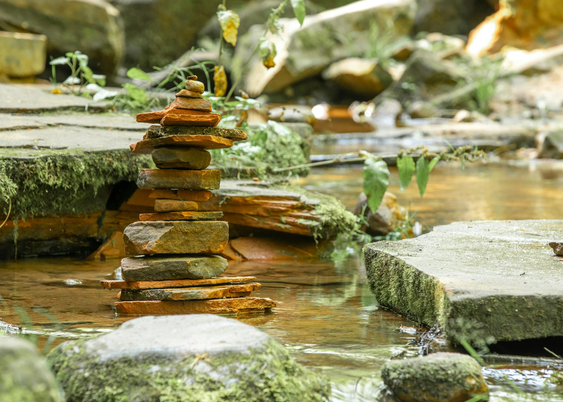 a pile of rocks sitting on top of a river, inspired by Andy Goldsworthy, unsplash, environmental art, las pozas, totem pole, ponds of water, brown