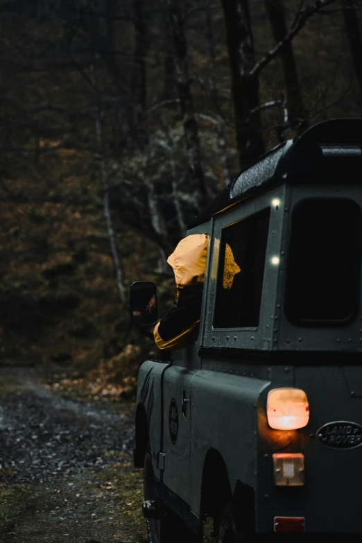 a car that is sitting on the side of a road, by Sebastian Spreng, unsplash contest winner, land rover defender 110 (1985), yellow raincoat, cabin lights, mossy head