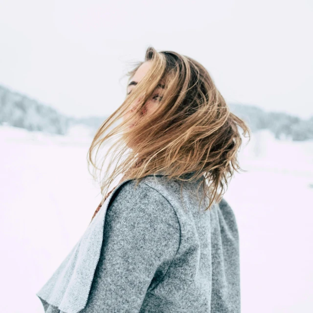 a woman standing in the snow with her hair blowing in the wind, trending on pexels, grey sweater, minimalistic art, looking from behind, girls