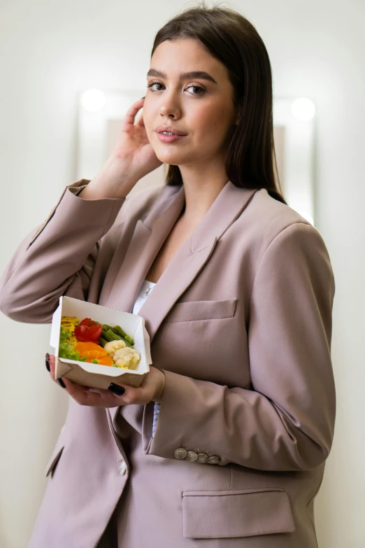 a woman talking on a cell phone while holding a plate of food, wearing a blazer, professional, soft, veggies