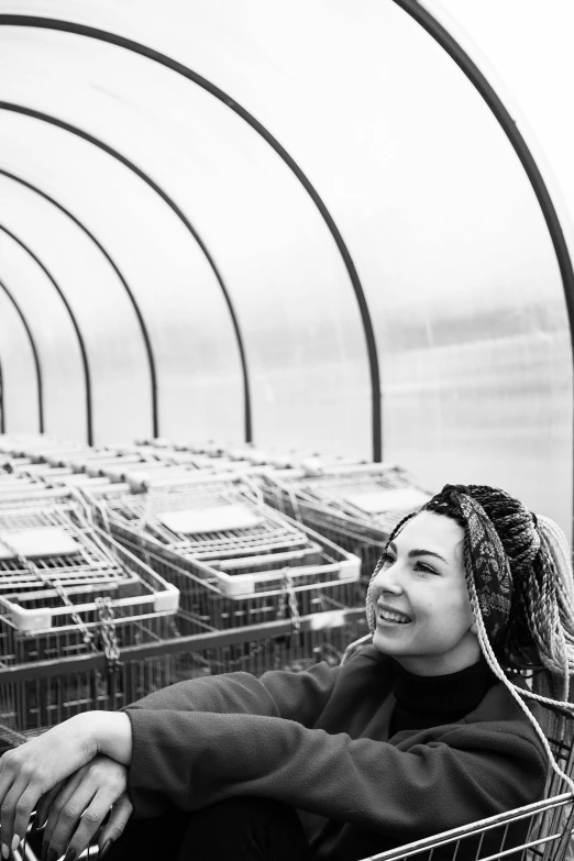 a black and white photo of a woman sitting in a shopping cart, bjork smiling, greenhouse, looking towards the horizon, profile image