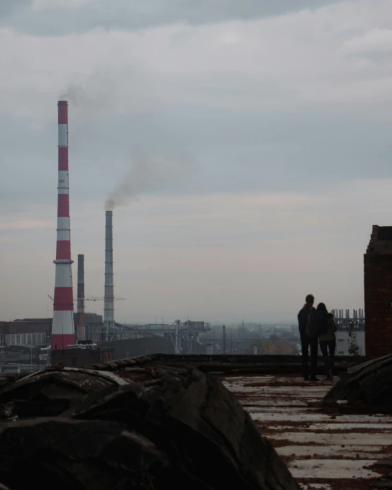 a couple of people standing on top of a roof, by Attila Meszlenyi, pexels contest winner, socialist realism, industrial plant environment, chimney, low quality photo, 15081959 21121991 01012000 4k