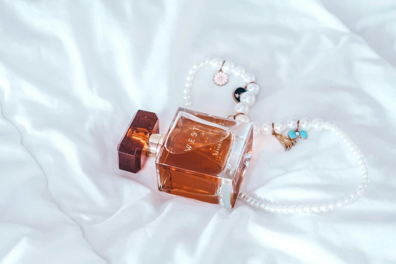 a bottle of perfume sitting on top of a bed, by Emma Andijewska, pexels contest winner, jewelry pearls, caramel, lv, peach embellishment