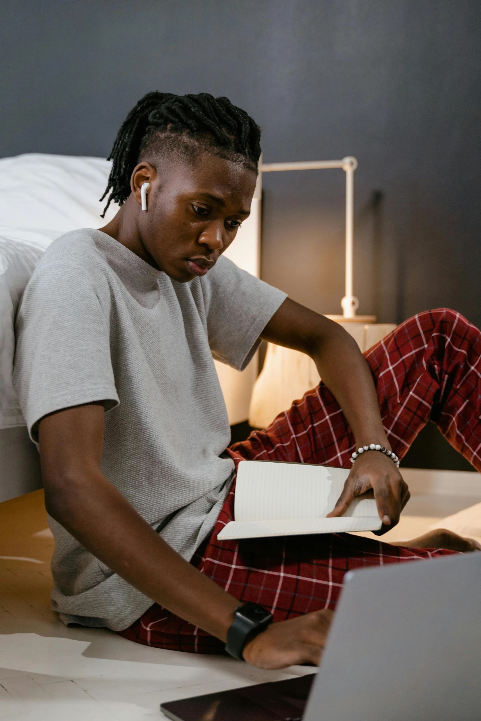 a man sitting on a bed using a laptop computer, by artist, trending on pexels, black teenage boy, reading a book, androgynous person, wearing a baggy pajamas