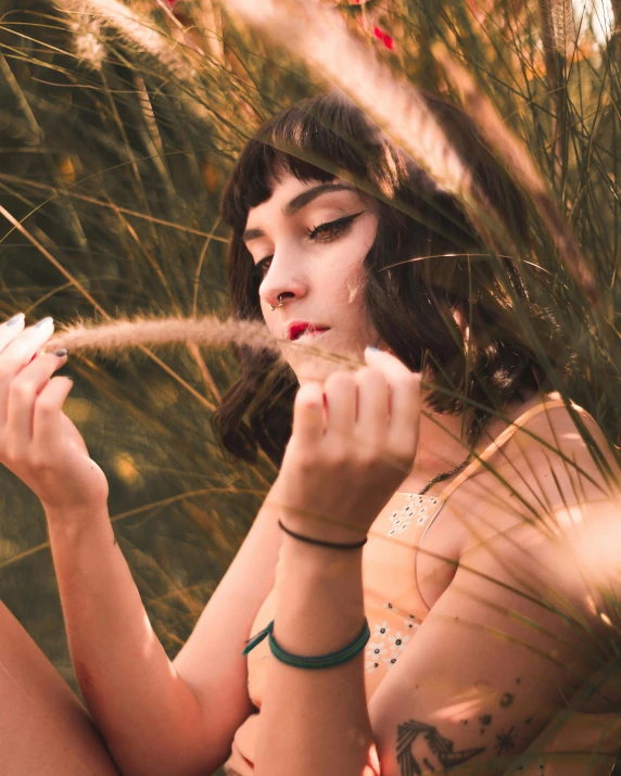 a woman sitting on the ground smoking a cigarette, an album cover, inspired by Elsa Bleda, trending on pexels, magic realism, lush grass, arya stark as venus, standing in tall grass, photo of a hand jewellery model