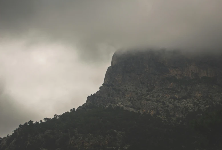 a tall hill covered in clouds and some tree on top