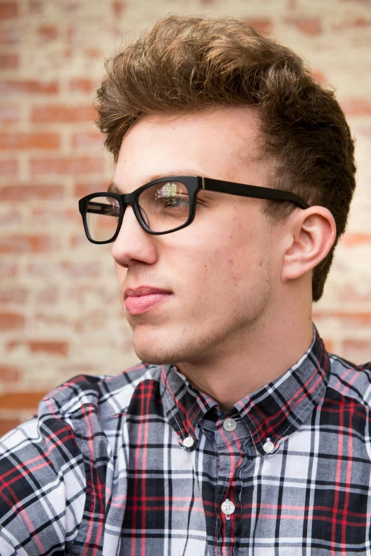 a young man wearing glasses sitting in front of a brick wall, shutterstock, photorealism, half - frame square glasses, rhett and link, high resolution image, dynamic closeup