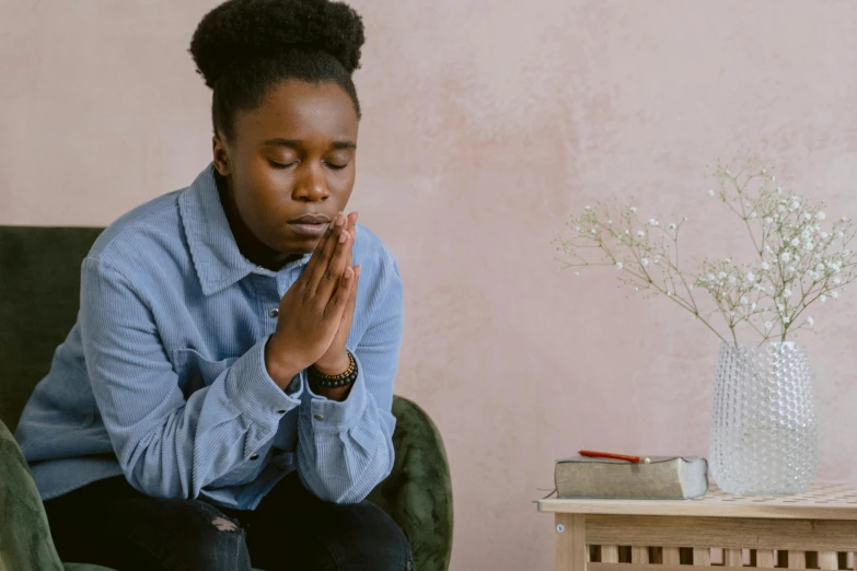 a woman is sitting in a chair and praying, trending on pexels, hurufiyya, black teenage boy, sitting on a table, restoration, annoyed