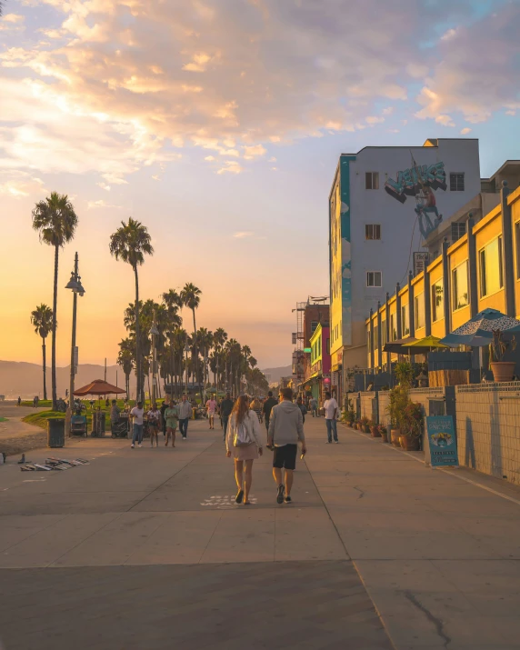 a group of people walking down a sidewalk, which shows a beach at sunset, colorful buildings, los angelos, profile image