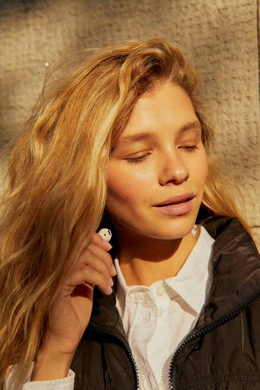 a woman holding a cell phone to her ear, by Christen Dalsgaard, model wears a puffer jacket, flowy golden hair, sunbathed skin, no makeup wavy hair