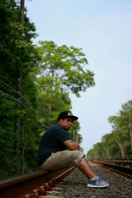 a man sitting on a rail road track, inspired by Rudy Siswanto, sumatraism, angkor thon, trees in background, looking serious, slightly minimal