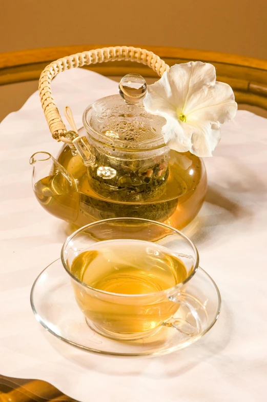 a tea pot sitting on top of a table next to a cup of tea, jasmine, thumbnail, golden glow, hibiscus